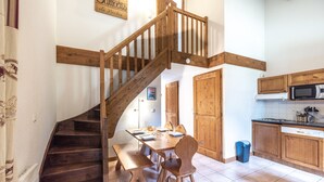 A kitchen with wooden cabinets, a dining table with chairs, a wooden staircase, and a microwave.