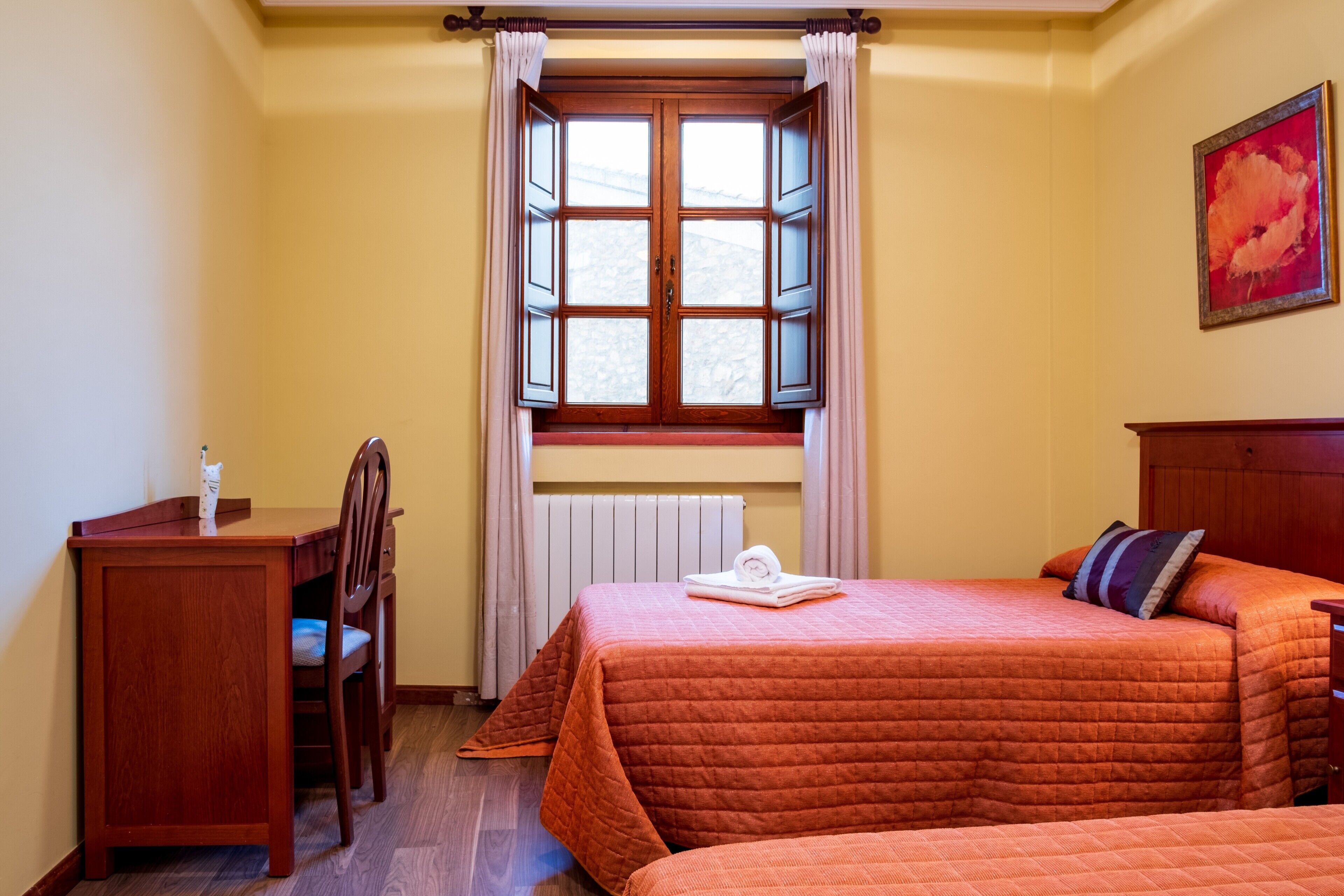 A room with a bed, a desk, a chair, a window with curtains, and a radiator.