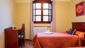 A room with a bed, a desk, a chair, a window with curtains, and a radiator.