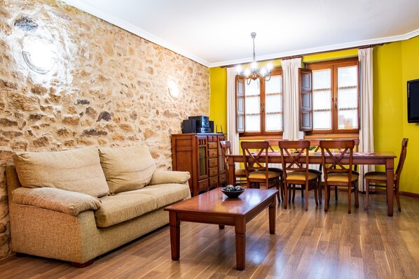 A living room with a stone wall, wooden furniture, a dining table, and a TV mounted on the wall.