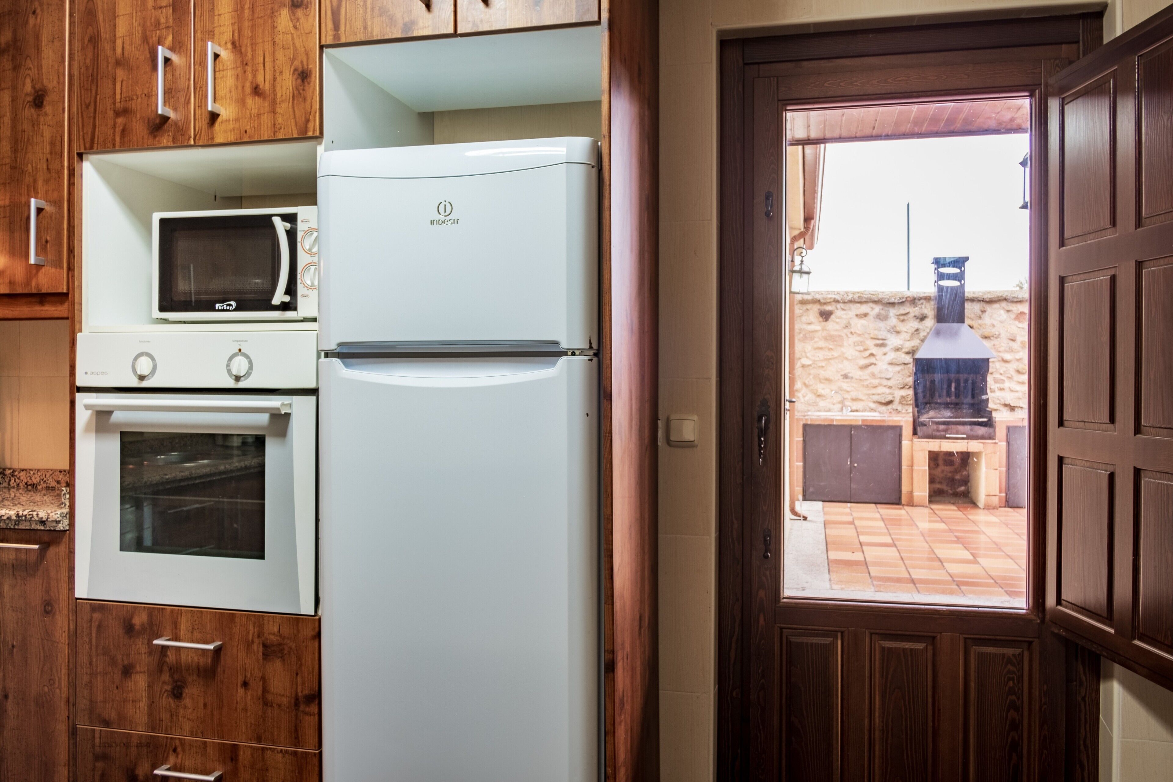 Eine Küche mit Kühlschrank, Mikrowelle, Backofen und Holzschränken.