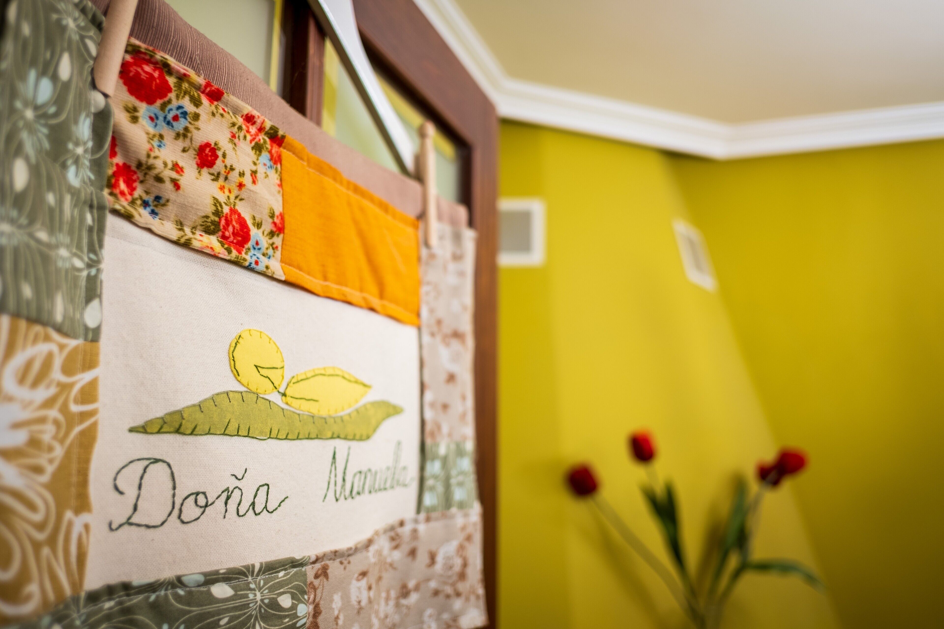 Una stanza con un letto rivestito di tessuto floreale, una targhetta e un vaso con fiori rossi.