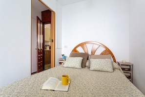 A bedroom with a wooden headboard, a bed with floral bedding, a bedside table with a lamp, and a door leading to another room.