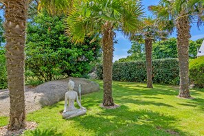 A garden with palm trees, a large rock, and a statue. - Holiday Home 'Maison Avec Spa À 700m De La Plage' with Private Terrace, Private Garden and Wi-Fi (Porspoder)