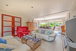 A spacious living room with a red armchair, white sofa, and a television. - Holiday Home 'Maison Avec Spa À 700m De La Plage' with Private Terrace, Private Garden and Wi-Fi (Porspoder)
