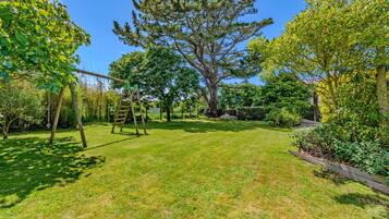 Un jardín bien cuidado con un columpio, un árbol grande y una cerca de madera.