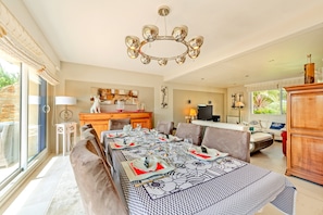 A dining area with a long table set for a meal, a chandelier, and a view through large windows. - Holiday Home 'Maison Avec Spa À 700m De La Plage' with Private Terrace, Private Garden and Wi-Fi (Porspoder)