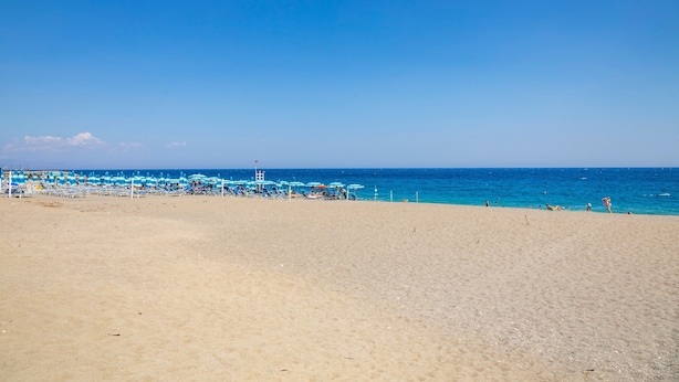 Une plage de sable, avec quelques parasols et un poste de surveillance pour les sauveteurs.