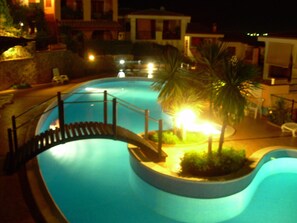 Una piscina con un puente, palmeras y un edificio al fondo.