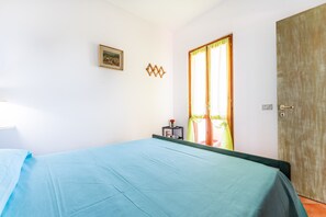 Un dormitorio con cama, una ventana con cortinas, una puerta y una mesita con un jarrón.
