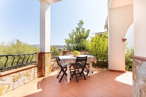 Un patio con una mesa, sillas, una planta en maceta y vistas a árboles y colinas.