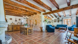 A spacious living area with a stone wall, wooden beams, a dining table with chairs, a blue sofa, and a fireplace. - Villa 'Toni Mosca' with Mountain View, Wi-Fi and Air Conditioning (Pollensa / Pollença)