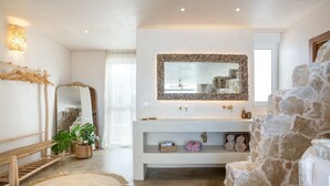Ein modernes Badezimmer mit Wandverkleidung aus Stein, einem großen Spiegel und einer integrierten Ablage mit Handtüchern und Dekoration.