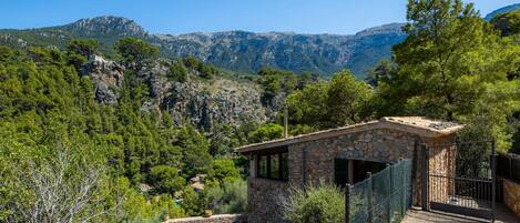 A stone building with a stone staircase, a fenced area, and a view of mountains.