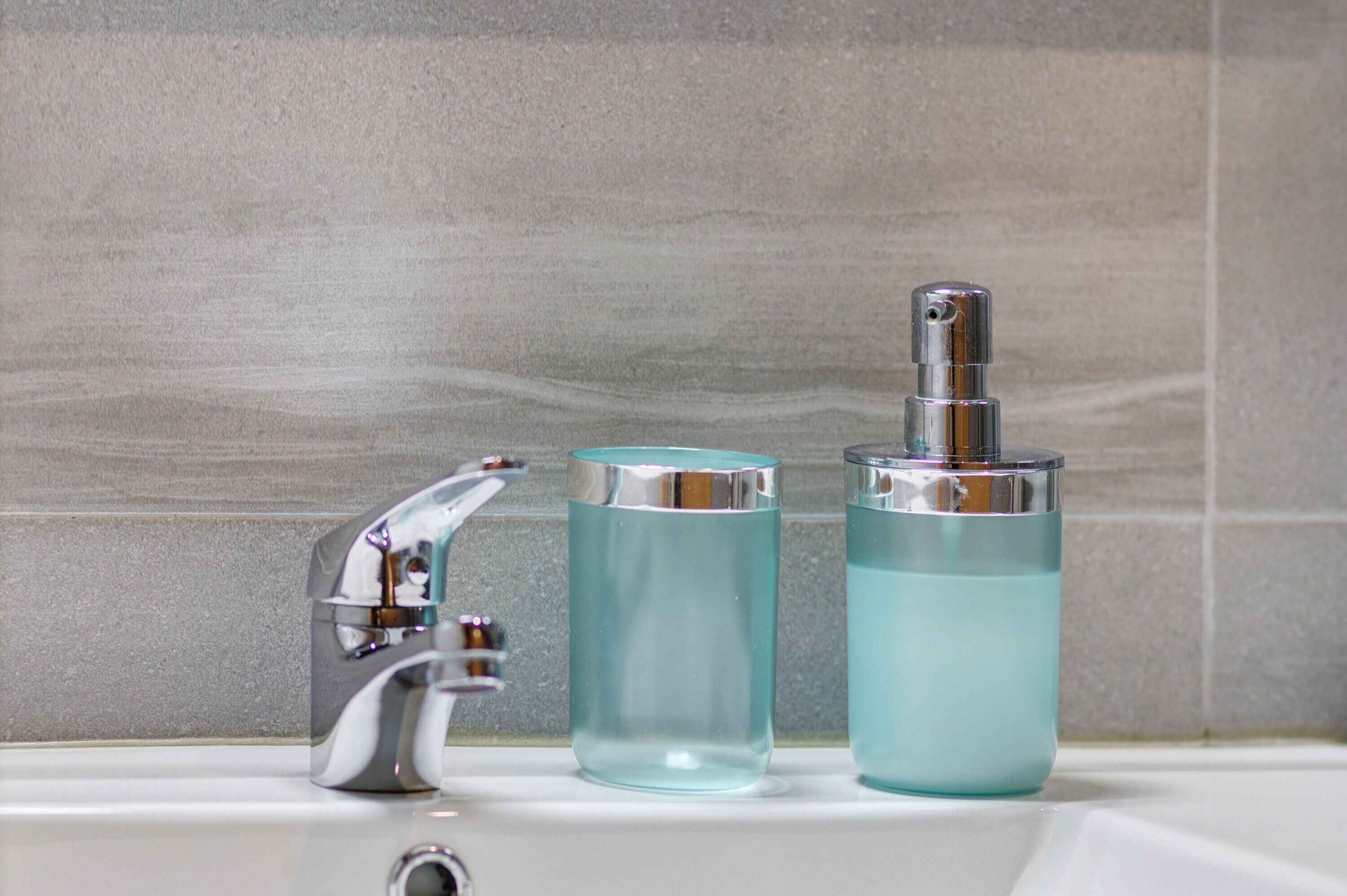 A bathroom with a chrome faucet, a clear glass bottle, and a larger glass bottle with a pump.