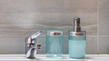 A bathroom with a chrome faucet, a clear glass bottle, and a larger glass bottle with a pump.
