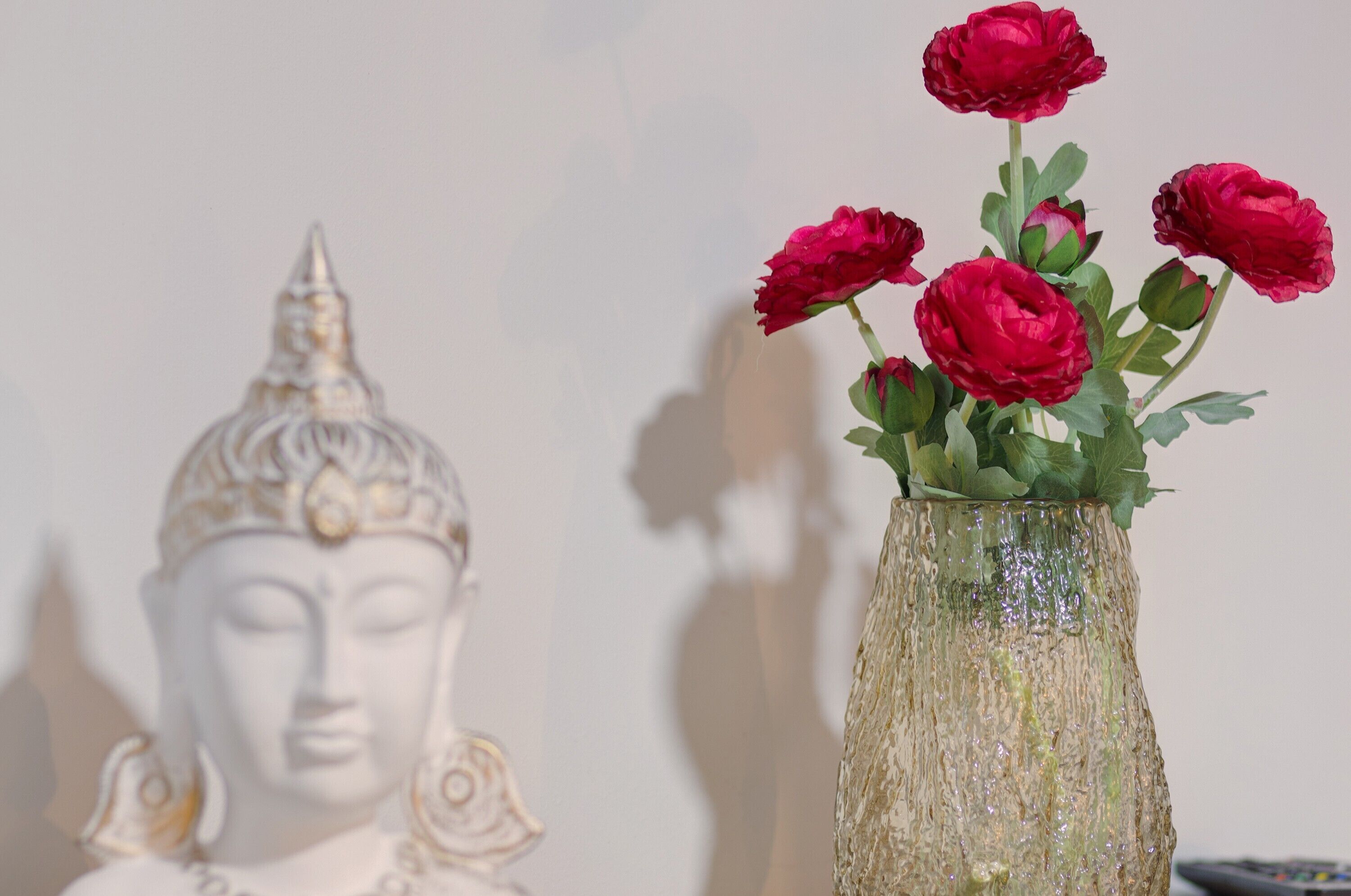 Eine Buddha-Statue und eine Vase mit roten Blumen.
