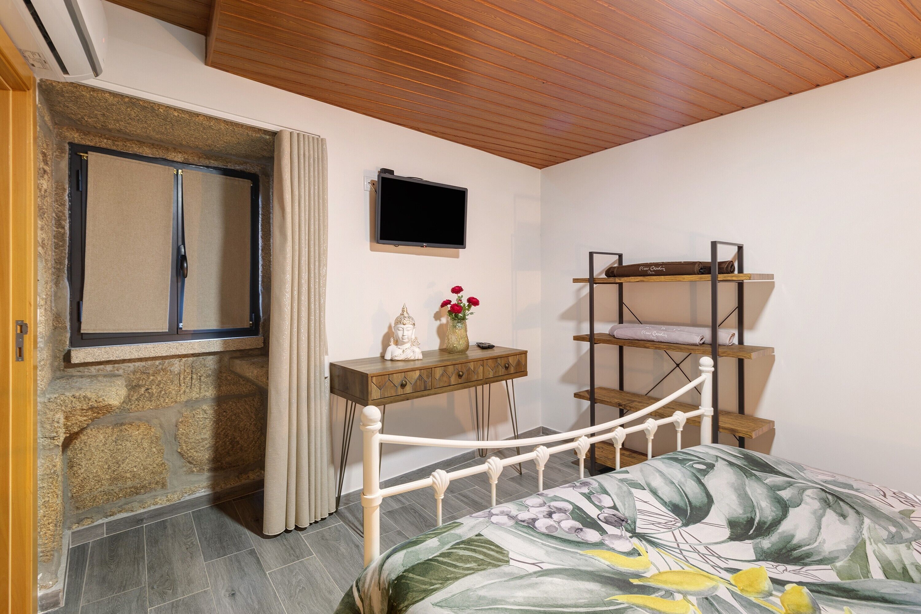 Ein Schlafzimmer mit einem Bett, einem Fernseher, einem kleinen Tisch mit einer Statue, einem Regal und einer Steinsäule.