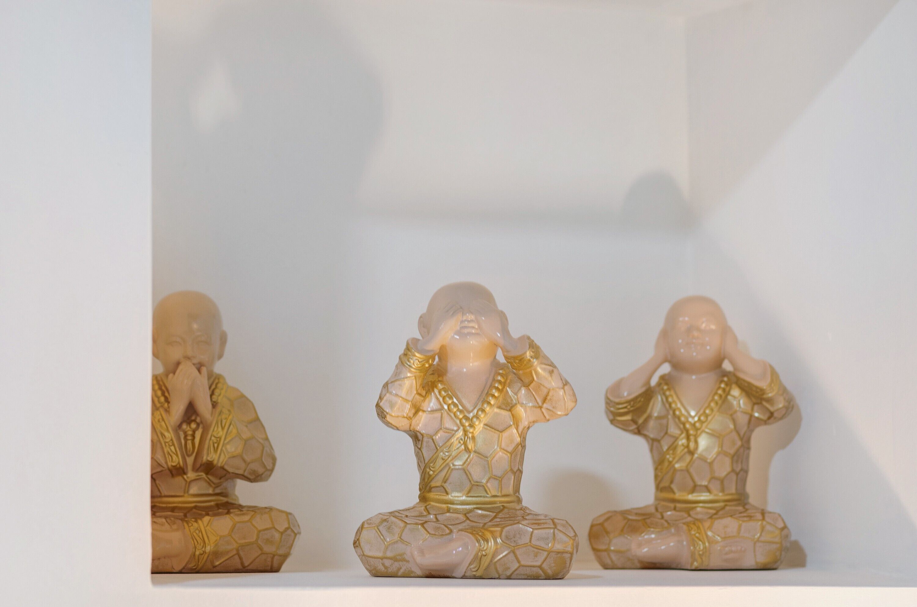 Tre statue raffiguranti una figura seduta con le mani in posizione di preghiera, esposte su uno scaffale.