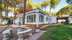 A white building with large windows, a stone bench, and a pergola with string lights. - Villa 'El Limonar' with Shared Pool and Wi-Fi (Chiclana de la Frontera)