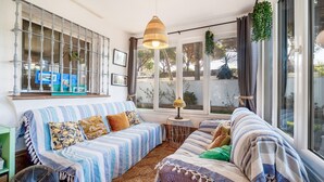 A cozy living room with a striped sofa, a fan, and a window with curtains. - Villa 'El Limonar' with Shared Pool and Wi-Fi (Chiclana de la Frontera)