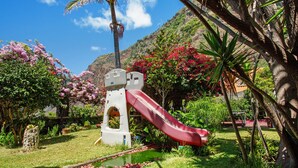 Un terrain de jeux avec un toboggan, entouré d’une végétation luxuriante et de plantes en fleurs.