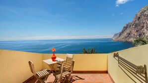 Un balcon avec une table et des chaises, offrant une vue sur la côte, la mer et une falaise.