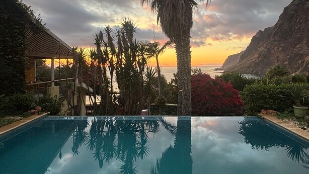 Une piscine avec vue sur le coucher de soleil, des palmiers et une montagne en arrière-plan.
