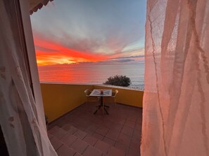 A balcony with a table and chairs, overlooking a sunset over the sea.