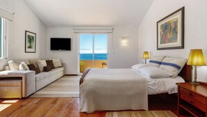Une chambre à coucher avec un lit, un canapé, une télévision, une fenêtre donnant sur un beau paysage et une lampe.