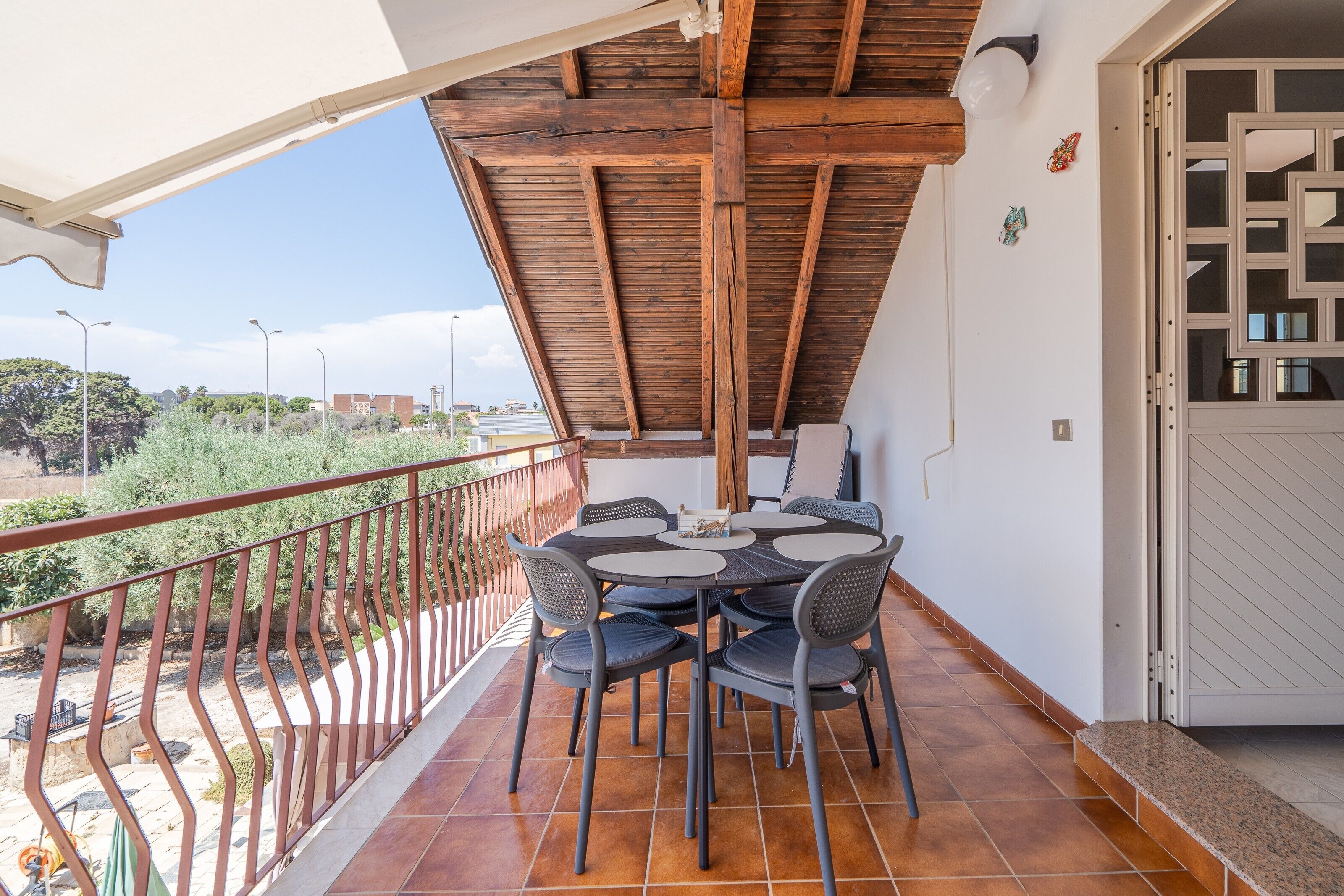 A balcony with a wooden ceiling, a round table with chairs, and a view of the surrounding area.