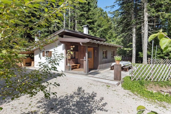 A small cabin with a wooden exterior, a porch, and a gravel driveway.