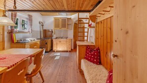 Un intérieur en bois comprenant une table à manger, des chaises, un banc, un coin cuisine avec des placards et un évier, ainsi qu’un plafond en bois.