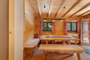 A wooden cabin interior with a dining table, bench, and kitchen area. - Chalet 'Laura' with Private Terrace and Private Garden (Cavareno)
