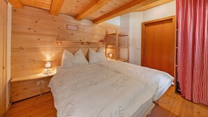 Une chambre dans une cabane en bois, avec un lit, des tables de chevet, une étagère et un rideau à carreaux rouges et blancs.