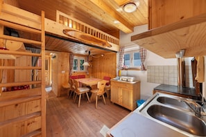 A wooden cabin interior with a dining area, kitchen, and a loft bedroom.