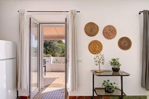 A room with a glass door leading to an outdoor area, a small table with a potted plant, and decorative woven wall hangings.