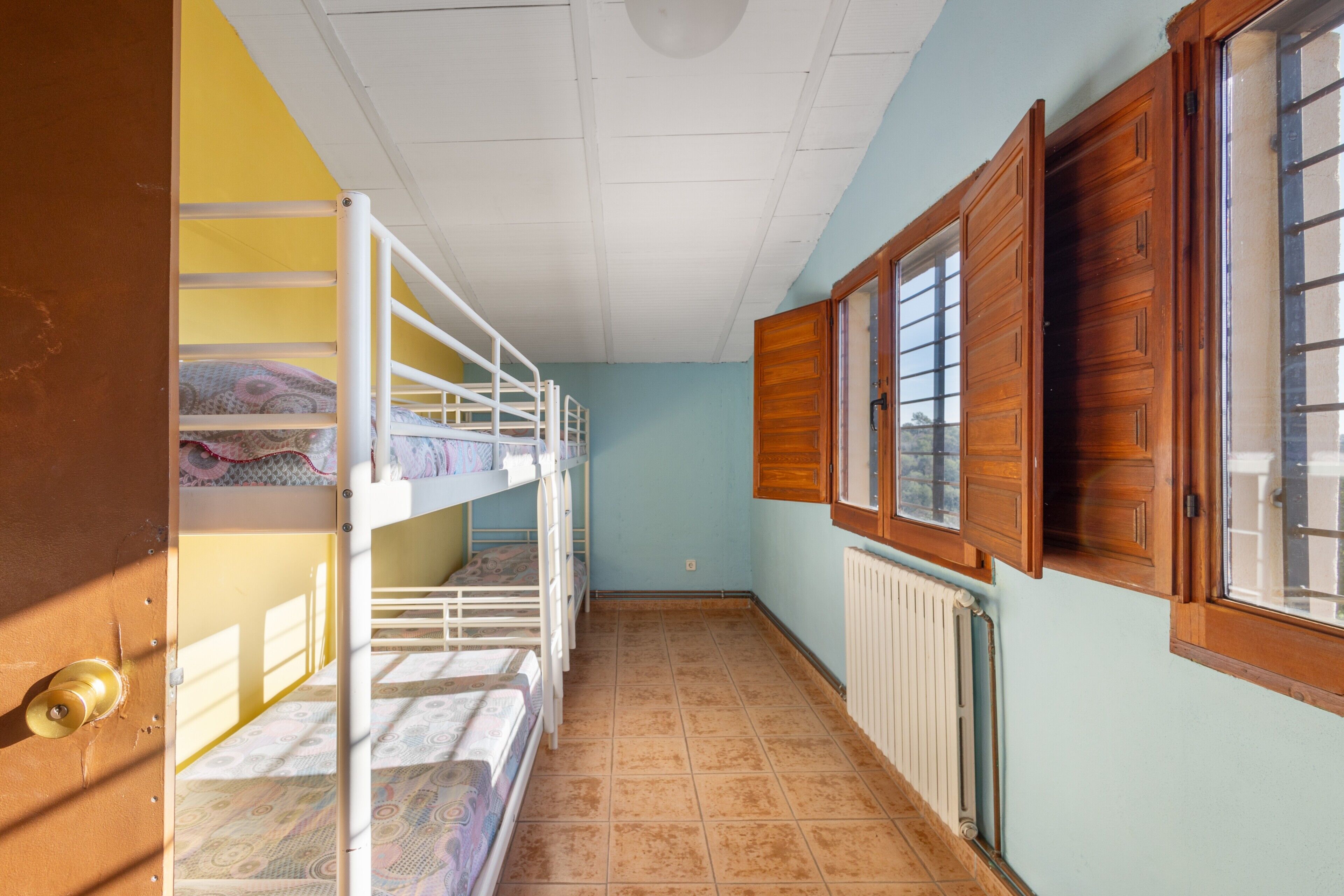 A narrow hallway with bunk beds, a radiator, and wooden shutters on the windows.
