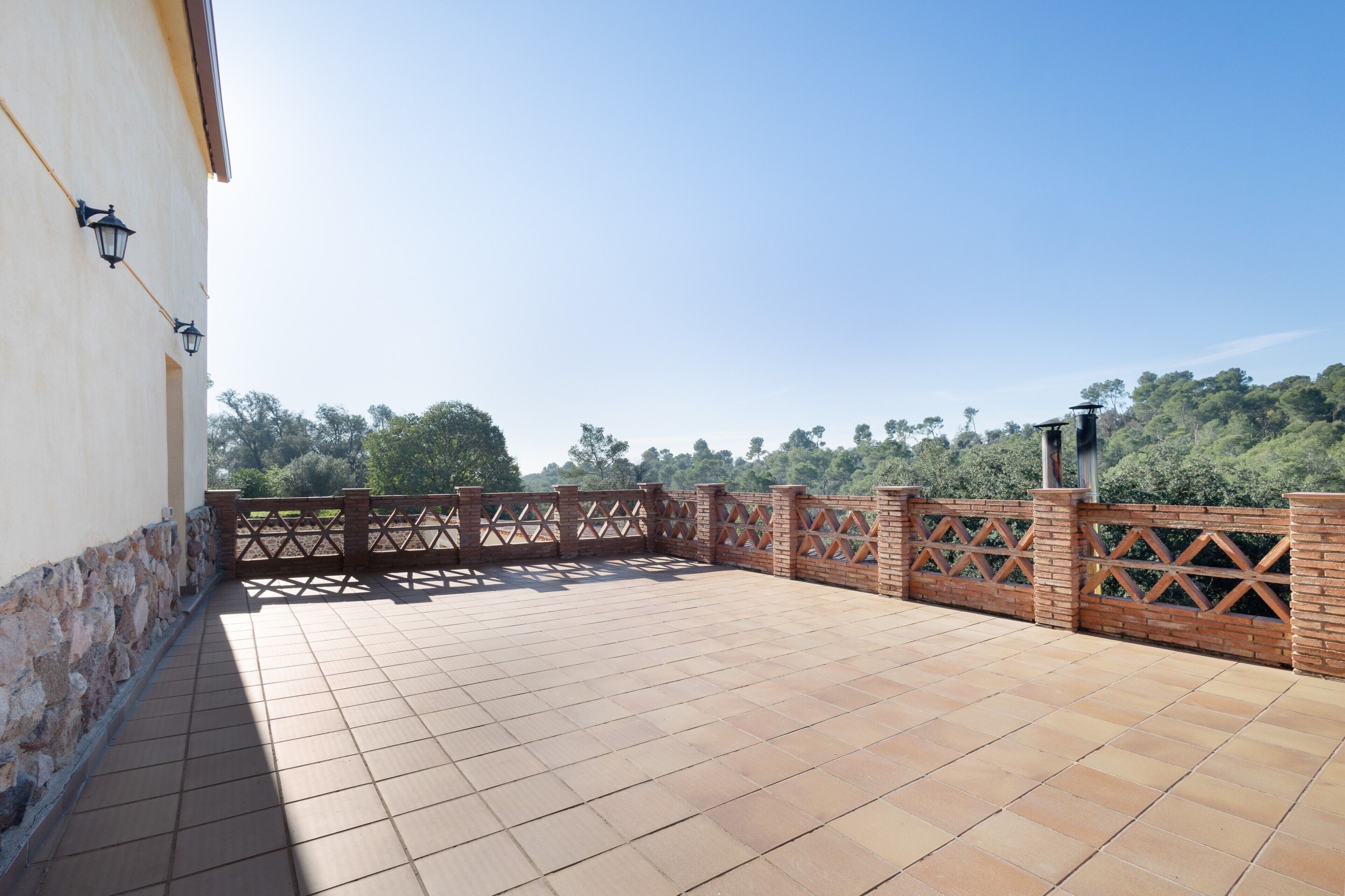 Eine Dachterrasse mit Fliesenboden, Ziegelwänden und einem Holzzaun.