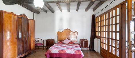 A bedroom with a wooden ceiling, a bed with a quilt, a wardrobe, and a window with a view.