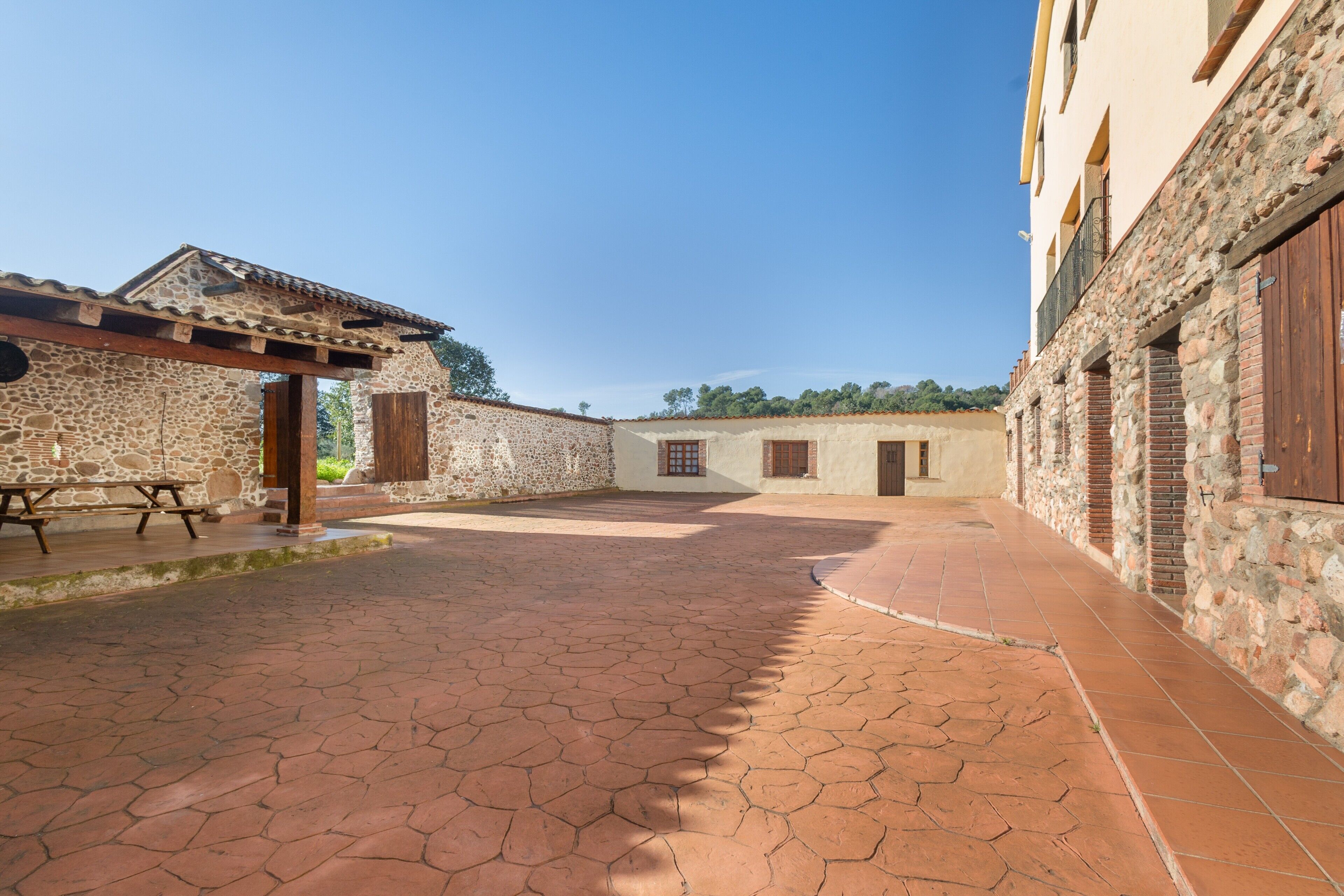 A courtyard with stone walls, a tiled floor, and a wooden pergola.