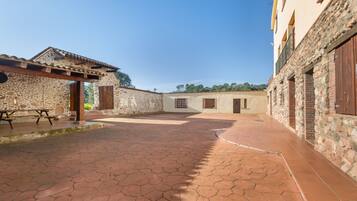 A courtyard with stone walls, a tiled floor, and a wooden pergola.