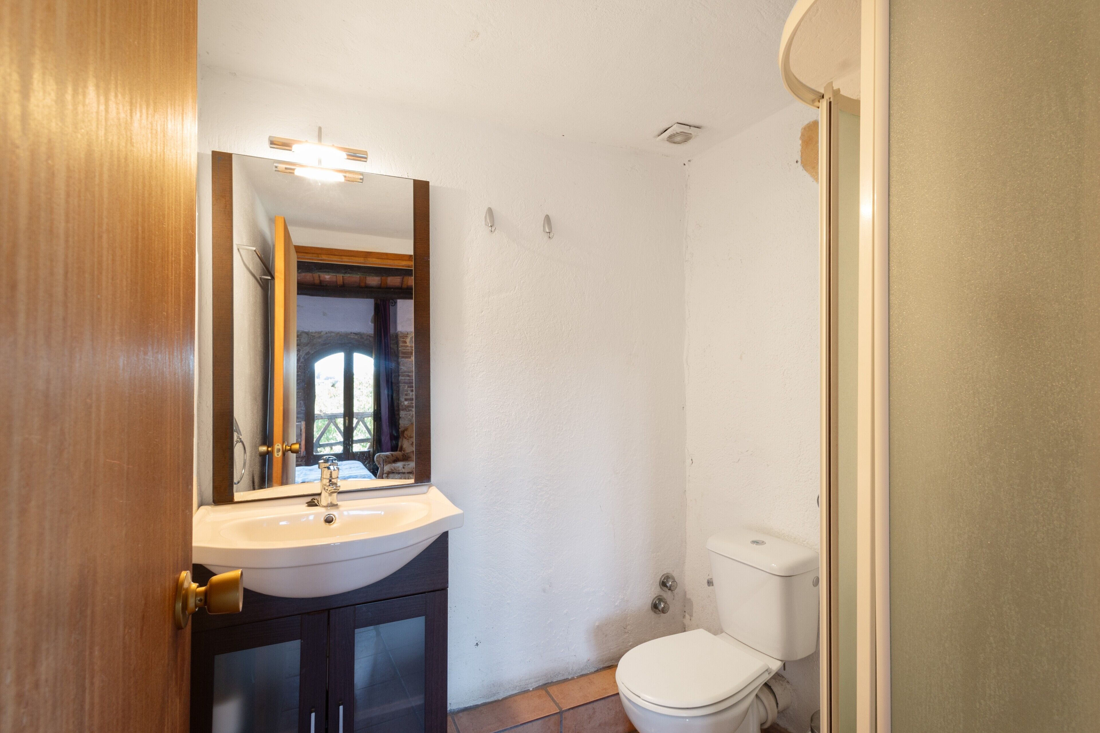 Ein Badezimmer mit Waschbecken, Spiegel, Toilette und Holztür.