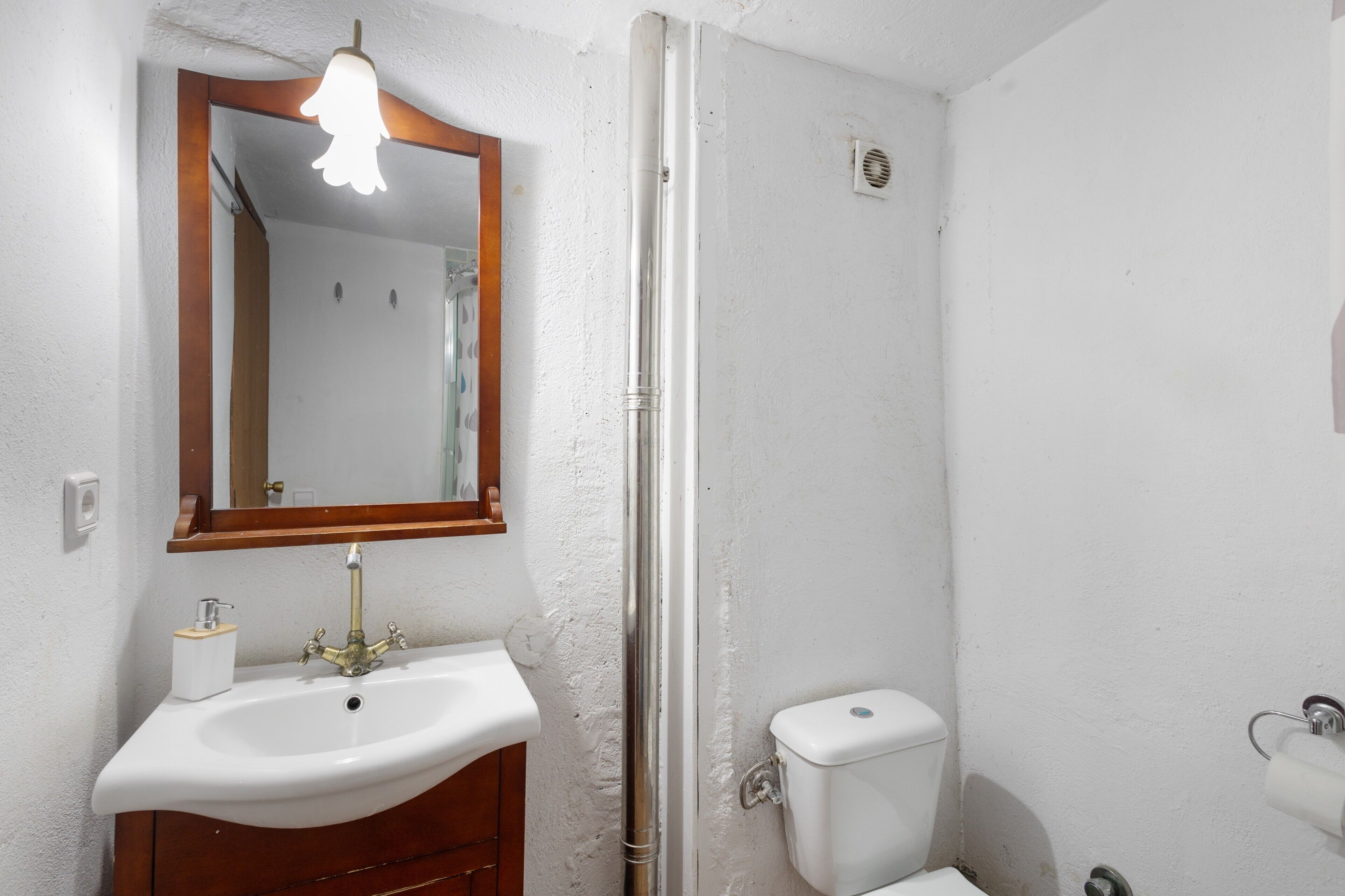 Un baño con lavamanos blanco, un espejo con marco de madera, inodoro y puerta de ducha.