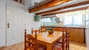 A dining area with a wooden table and chairs, a kitchen in the background, and a white door. - Country House 'Caseta Montanyana' with Private Terrace, Private Garden and Wi-Fi (Deltebre)