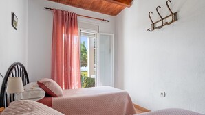 A bedroom with two beds, a window with curtains, a wall-mounted hook, and a lamp on a bedside table. - Country House 'Caseta Montanyana' with Private Terrace, Private Garden and Wi-Fi (Deltebre)