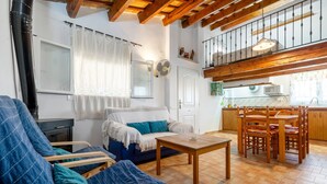 A cozy living room with a sofa, chairs, a wooden table, and a kitchen area with a dining set. - Country House 'Caseta Montanyana' with Private Terrace, Private Garden and Wi-Fi (Deltebre)
