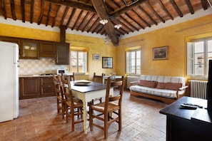 Une cuisine spacieuse avec des meubles en bois, une table à manger et des chaises. Le salon comprend un canapé et un téléviseur.