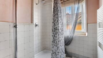 Eine Dusche mit Duschvorhang, ein Fenster mit Ausblick und ein gefliester Boden.