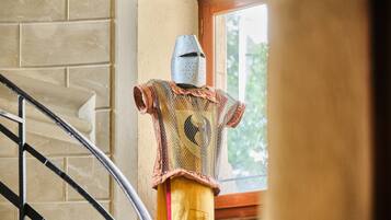 A medieval knight's armor displayed indoors, a staircase, and a window with a view of greenery.